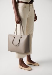 Gray leather tote bag with two shoulder straps and gold hardware details. The bag features a structured design and a smooth texture.