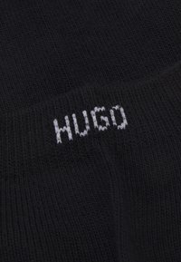 Calcetines negros con textura acanalada, que presentan un logo bordado en blanco de "HUGO" en el puño. Material suave, diseñado para la comodidad y durabilidad.