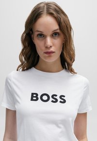 White cotton t-shirt featuring bold black "BOSS" print on the front, classic round neck, and short sleeves. Smooth texture.