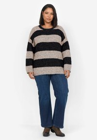 Striped sweater in beige and black, oversized fit with long sleeves, paired with blue jeans and brown ankle boots. Soft, textured fabric.