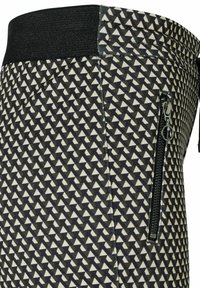 Schwarz- und cremefarbenes, geometrisch gemustertes Gewebe mit dreieckigen Formen; ausgestattet mit einem gerippten Taillenbund und einer mit Reißverschluss versehenen Tasche an der Seite.