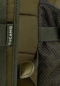 Rugzak van donkergroene stof, met gevoerde gedeelten, gaasdetails en een Tucano-label. Kenmerken zijn verstelbare banden en een glad leren accent.