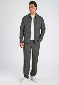 Grijze textuur jas met twee borstzakken, gedragen over een wit t-shirt, gecombineerd met bijpassende grijze broek en witte sneakers.