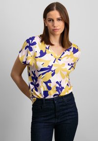 Kortærmet bluse med V-udskæring i et blomstermønster med lilla, gul og pink farver. Letvægtsstof med en afslappet pasform.