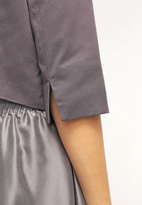 Gros plan sur le bras d'une personne portant un haut gris à manches courtes avec une fente latérale et une jupe grise brillante et froncée.