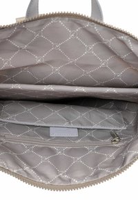 Interior de bolsa gris claro con un patrón acolchado decorativo que presenta líneas punteadas y círculos. Un bolsillo con cremallera y un compartimento adicional para la organización.