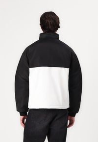 Black and white jacket with a high collar, elastic cuffs, and a color-block design. The fabric appears smooth with a slightly shiny finish.