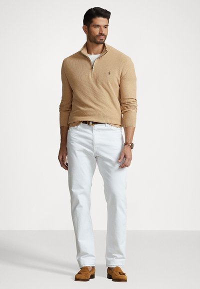Beige ritsvest, witte broek en bruine suède schoenen. Eenvoudig ontwerp met geribde manchetten. Klassieke pasvorm en neutraal kleurenschema.