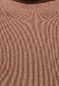 Rippstrickpullover in einem staubigen Rosaton, mit hohem Kragen und strukturiertem Stoff mit einem sanften Glanz. Nahaufnahme des Materials.