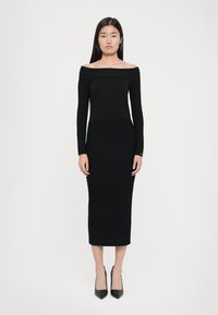 Musta ribbelly off-the-shoulder mekko, jossa on pitkät hihat, istuva yläosa ja polven pituinen helma. Yhdistetty teräväkärkisiin mustiin korkokenkiin.