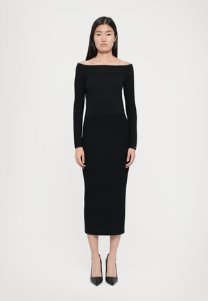 Musta ribbelly off-the-shoulder mekko, jossa on pitkät hihat, istuva yläosa ja polven pituinen helma. Yhdistetty teräväkärkisiin mustiin korkokenkiin.