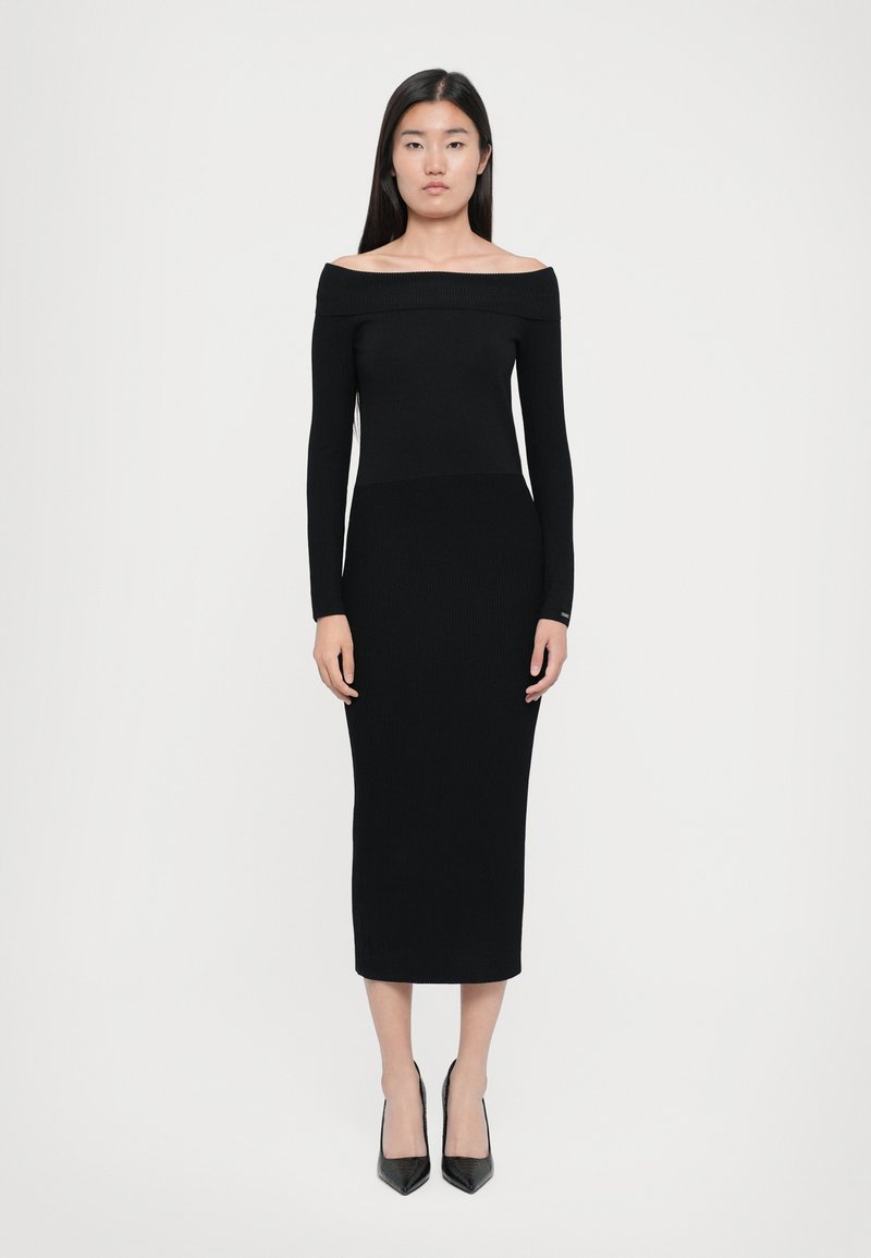 Musta ribbelly off-the-shoulder mekko, jossa on pitkät hihat, istuva yläosa ja polven pituinen helma. Yhdistetty teräväkärkisiin mustiin korkokenkiin.