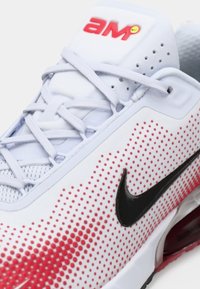 Nike sneakers con un design a pois bianchi e rossi, swoosh nero, texture a rete e chiusura classica a lacci.