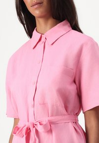 Rosa knappopp skjorte med krage, korte ermer, brystlomme og knyttet midje detalj. Laget av et mykt, teksturert stoff.