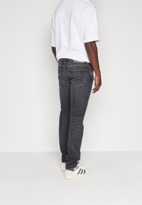 Grå denimjeans med slim fit, med bakfickor och en ljusbrun läderlapp. Bärs med en lösvit t-shirt och vita sneakers.