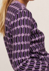 Maglione viola con motivo a diamante geometrico con accenti neri, realizzato in materiale lavorato a maglia, con maniche lunghe e scollo rotondo.