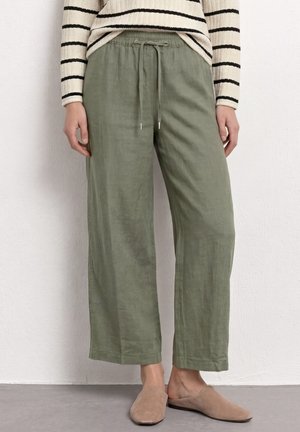 Pantalon ample vert olive clair avec taille à cordon, porté avec des chaussures beiges à enfiler et un pull rayé noir et blanc.