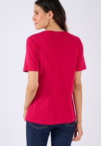 Camiseta ajustada de manga corta en algodón rosa brillante, con cuello redondo y dobladillo recto, combinada con unos vaqueros de denim azul oscuro.