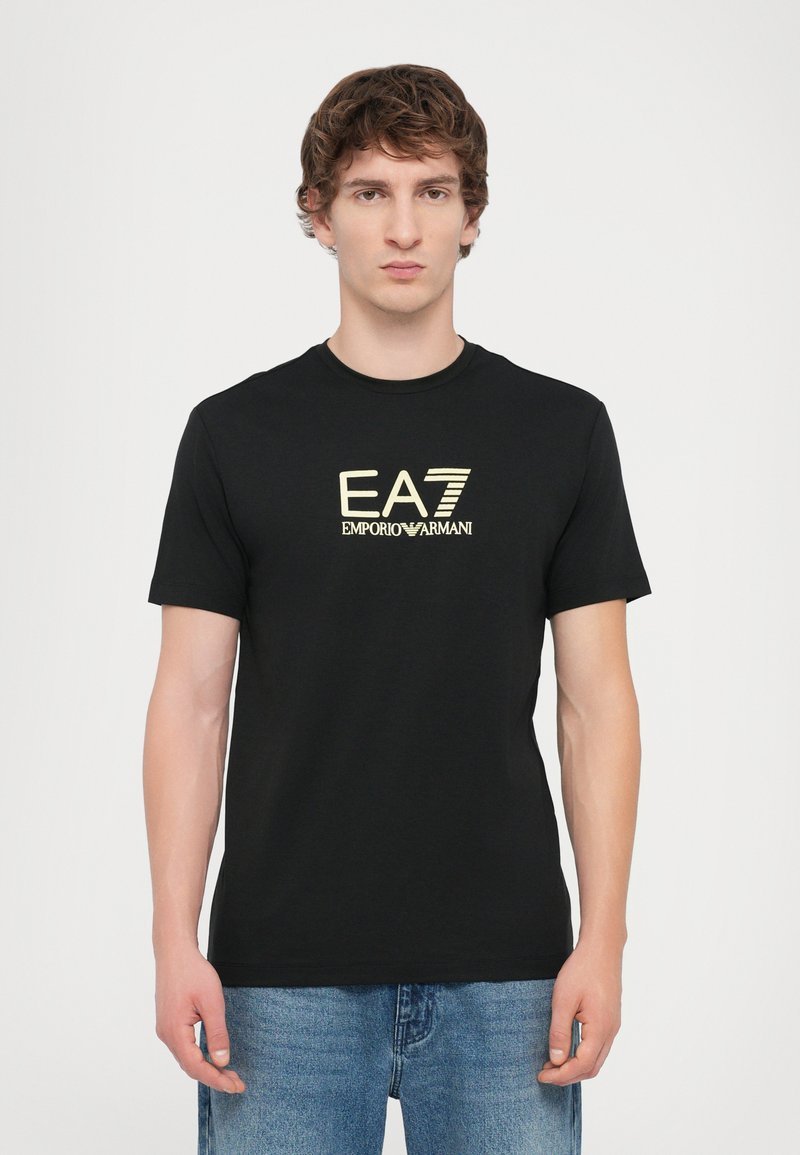 T-shirt de algodão preto com o logotipo dourado EA7 Emporio Armani no peito. Mangas curtas e um decote redondo clássico.