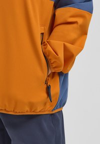 Giacca a blocchi di colore arancione e blu, con tasca laterale con zip e una finitura morbida e texturizzata. Il design include polsini elasticizzati.