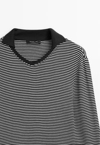 Black and white striped polo shirt with a black collar, featuring a v-neck design and soft fabric texture. Label visible inside the neckline.