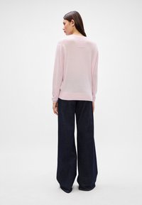 Ανοιχτό ροζ πουλόβερ με χαλαρή γραμμή, ribbed μανσέτες και τελείωμα, συνδυασμένο με φαρδιά τζην παντελόνια σε σκούρο χρώμα, δημιουργώντας μια αντιθετική χρωματική παλέτα.