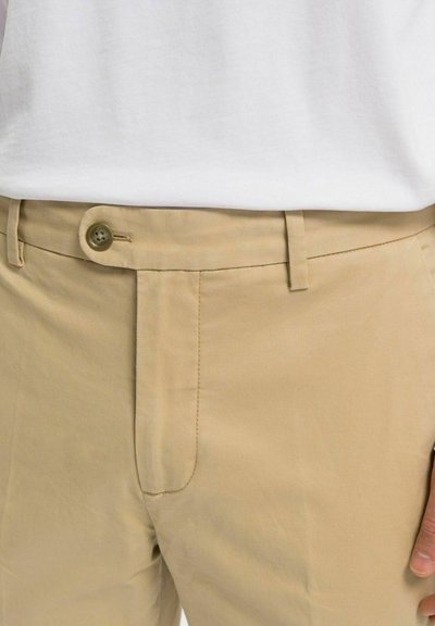 Beige chinos tillverkade av en bomullsblandning; har en framknappringning, bältesömmar och framfickor med en slät struktur.