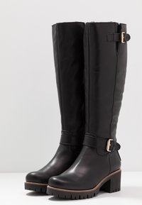 Botas de cuero negro hasta la rodilla con un tacón grueso, que cuentan con un acento de hebilla lateral y una suela texturizada para un mejor agarre. Acabado suave.