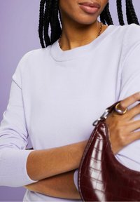 Světlofialový svetr s kulatým výstřihem a žebrovanými manžetami, doplněný vínově červenou kabelkou s krokodýlím vzorem.