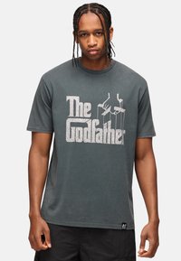 Grå bomulds t-shirt med korte ærmer, med hvidt "The Godfather" tryk og grafik af hænder, der holder marionettråde på forsiden.