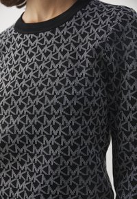 Maglione nero con motivo geometrico bianco, dotato di colletto rotondo a costine e tessuto strutturato. La vista ravvicinata evidenzia i dettagli del design.