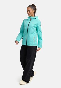 Turquoise insulated jacket with a hood, front zipper, and side pockets; paired with black wide-leg pants and light-colored sneakers.