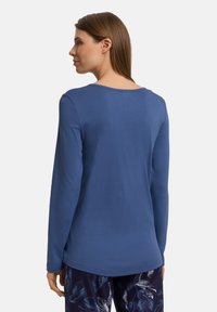 Top de manga larga azul en una tela suave y elástica con cuello redondeado; combinado con pantalones oscuros estampados que presentan diseños de hojas claras.