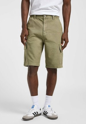 Olivengrøn cargo shorts med to sidelommer, lavet af robust stof. Har en knaplukning og bæltesløjfer. Båret med hvide sokker og sneakers.