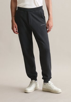 Zwarte joggingbroek gemaakt van zachte stof, met een trekkoord in de taille, zijzakken en een klein wit logo op de voorkant.