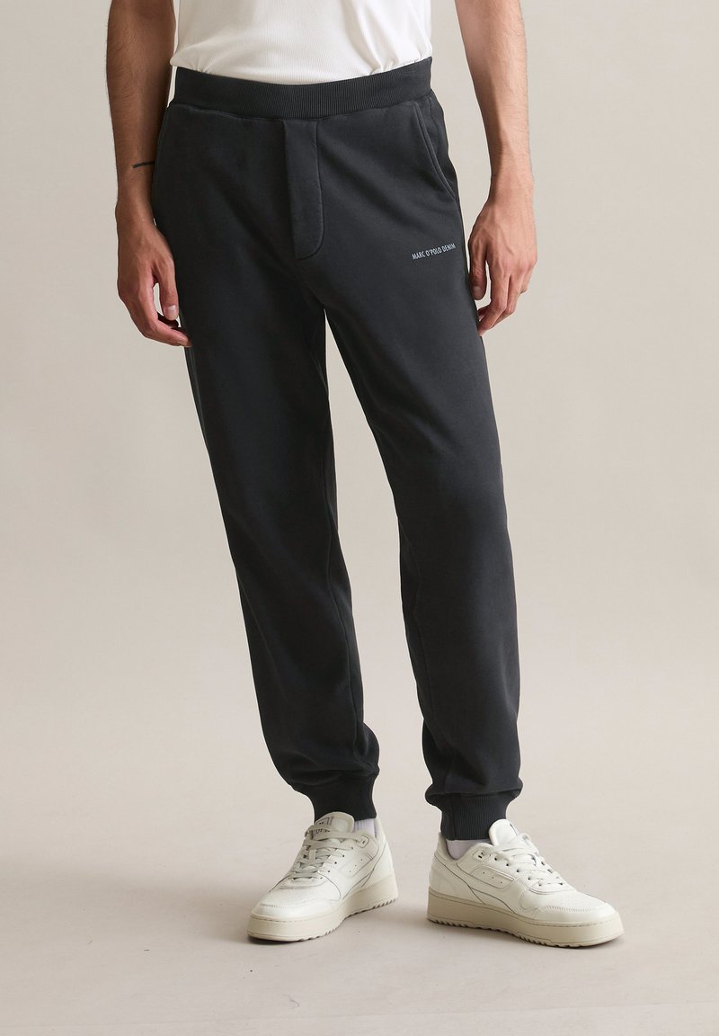 Zwarte joggingbroek gemaakt van zachte stof, met een trekkoord in de taille, zijzakken en een klein wit logo op de voorkant.