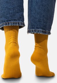 Żółte prążkowane bawełniane skarpetki o dopasowanym kroju, zestawione z przyciętymi niebieskimi dżinsami z postrzępionymi brzegami.