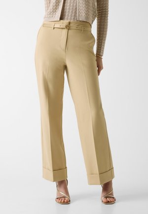 Beige, hoch taillierte Hose mit Bügelfalte vorne und umgeschlagenen Säumen, getragen mit Riemchen-Sandaletten mit hohem Absatz und einem gestrickten Oberteil.