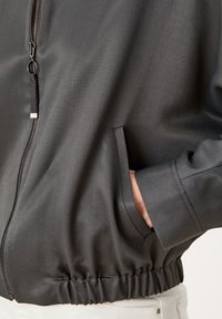 Veste noire à fermeture éclair avec une finition texturée, une taille élastique et des poches latérales. Dotée d'un tirette de fermeture éclair contrastant.