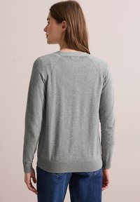 Pull en maille gris clair avec des manches longues, un col ras du cou et des poignets côtelés. Texture douce et coupe décontractée. La vue de dos montre un design d'épaule sans couture.