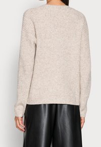 Pull beige en tricot avec un motif texturé, épaules tombantes et poignets côtelés, associé à un pantalon large en cuir noir.
