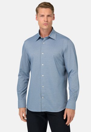 Camisa de manga larga azul claro con cuello extendido, textura sutil y botones en el frente; corte slim con dobladillo redondeado.