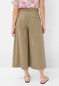 Pantalons larges kaki en tissu lisse, dotés de poches à l'arrière et d'une ceinture. Associés à des sandales légères, vus de l'arrière.
