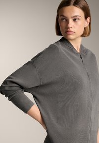 Grauer Reißverschluss-Pullover aus Strickstoff, mit gerippten Bündchen und seitlichen Einsätzen für eine lässige Passform. Minimalistisches Design mit glatter Textur.