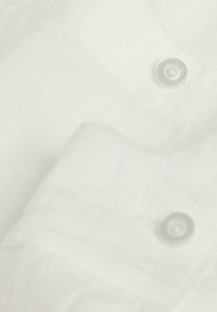 White linen shirt with a smooth texture, featuring light-colored buttons and a folded sleeve. Stitched edges visible.