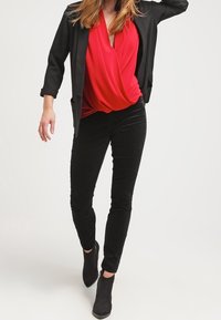 Červená zavinovací blůza, černý blazer, černé slim kalhoty a kotníkové boty. Blazer má strukturované ramena; blůza má splývavý design.