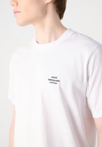 White cotton t-shirt featuring a crew neckline and short sleeves. Left chest has black embroidered text: "MADS NØRGAARD COPENHAGEN."