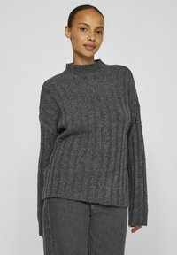 Grijze geribbelde gebreide trui met een hoge hals en lange mouwen, met een relaxte pasvorm en zachte textuur. Gecombineerd met donkere grijze broek.