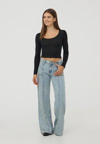 Czarny, długi rękaw, krótka bluzka zestawiona z jasnoniebieskimi, szerokimi spodniami dżinsowymi, które mają kontrastowe szwy, gładką fakturę i subtelny połysk materiału.