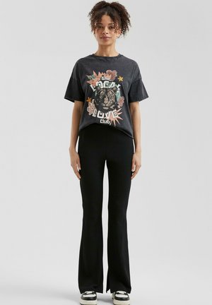 Zwarte graphic t-shirt met een tijgerdesign en bloemenaccenten, gecombineerd met zwarte flare broeken en zwart-witte sneakers.